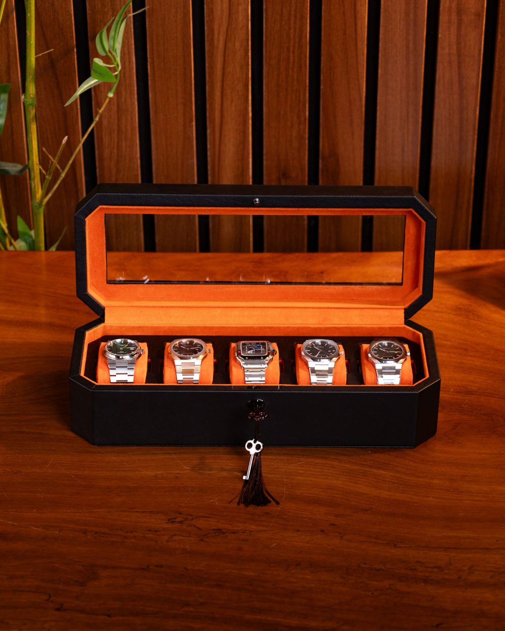 The Duchess open on a wooden table with five watches on orange cushions and a tassel key
